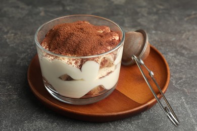 Delicious tiramisu in glass and sieve with cocoa powder on grey table