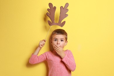 Cute little boy with reindeer antlers prop on yellow background. Christmas celebration