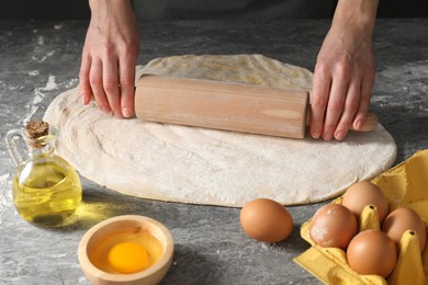 Photo of Woman rolling raw dough at grey table, closeup