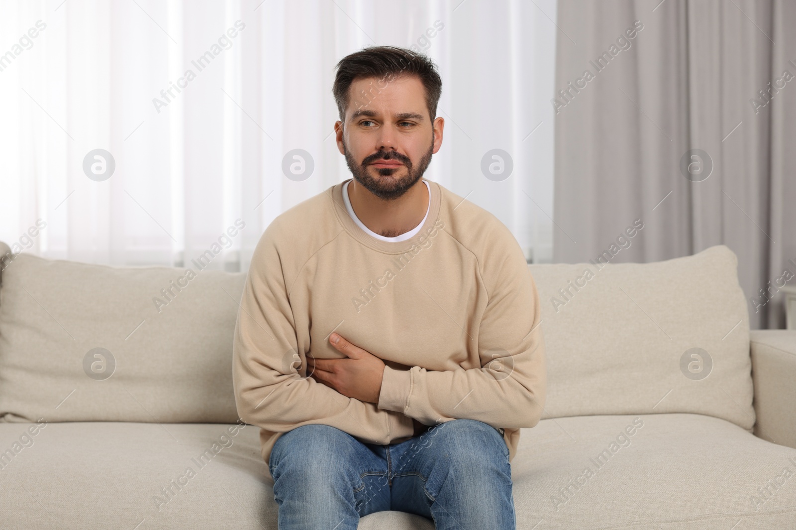 Photo of Man suffering from stomach pain on sofa at home