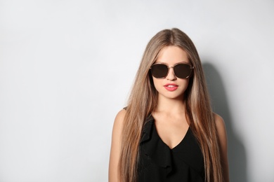 Photo of Young woman wearing stylish sunglasses on light background. Space for text