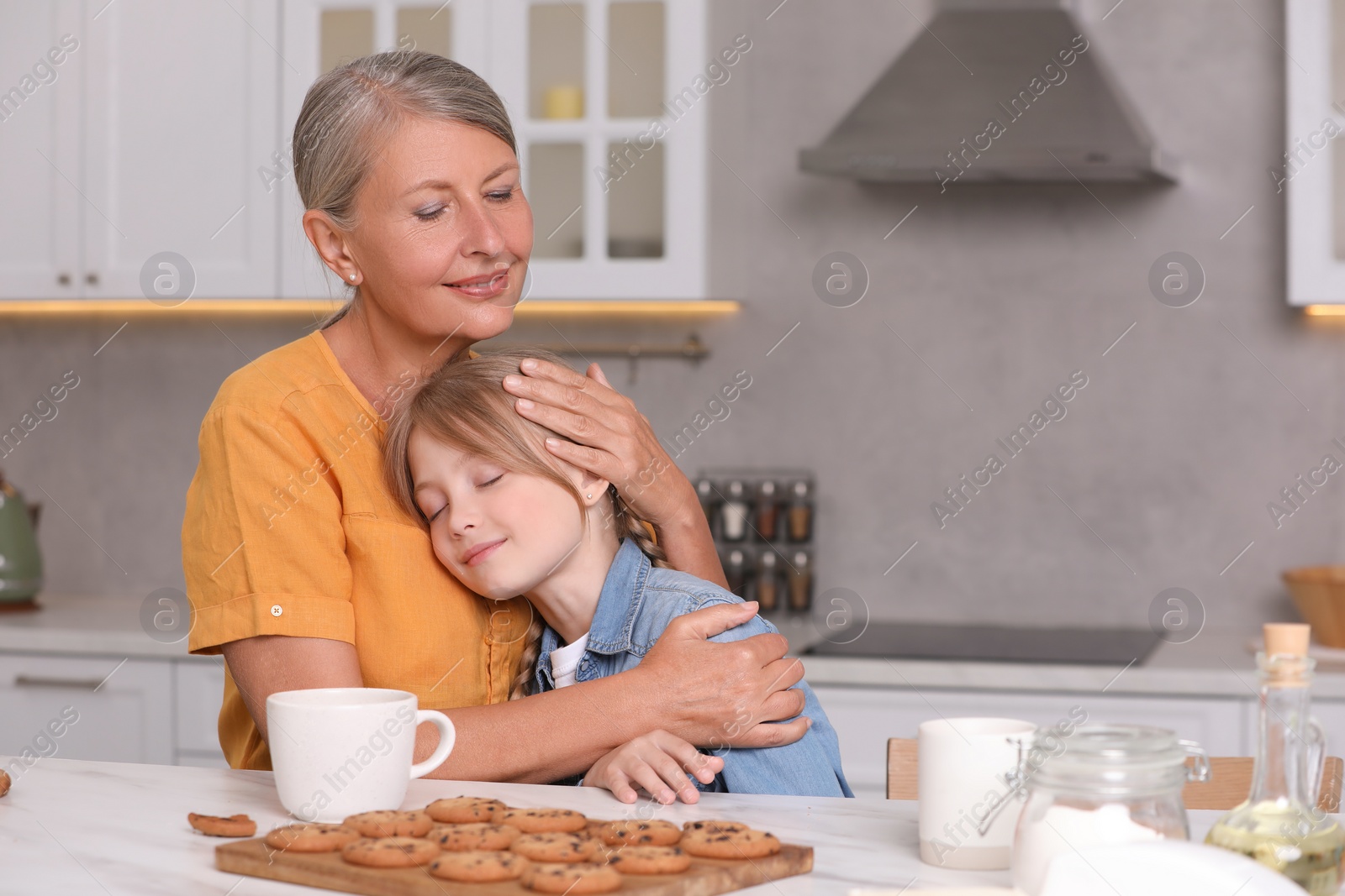 Photo of Happy grandmother hugging her granddaughter in kitchen