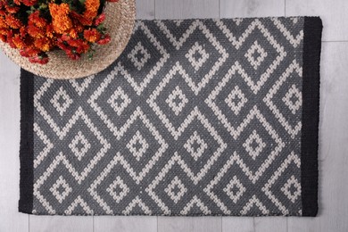 Photo of Stylish door mat with beautiful pattern and flowers on floor, flat lay