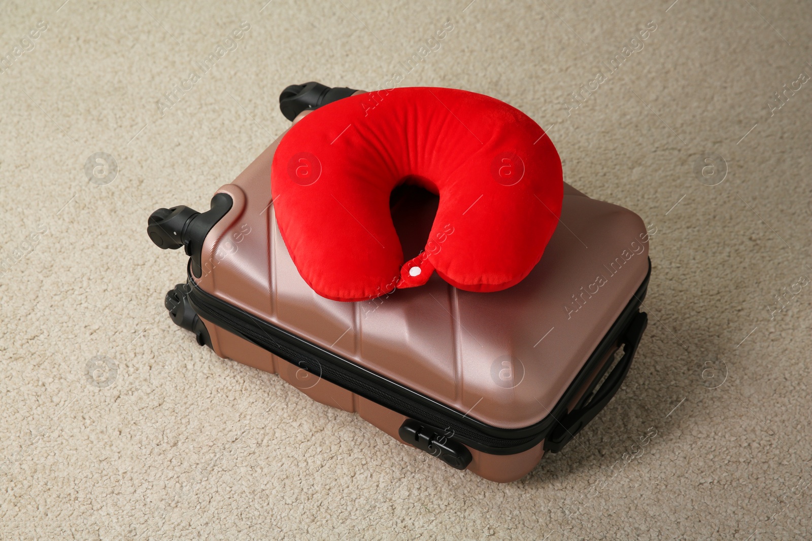 Photo of Red travel pillow and suitcase on beige rug