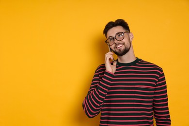 Photo of Handsome man in striped sweatshirt and eyeglasses talking on phone against yellow background, space for text