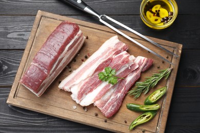 Photo of Pieces of raw pork belly, chili pepper, peppercorns, rosemary and parsley on black wooden table, flat lay