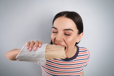 Young woman eating delicious shawarma on grey background