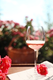 Photo of Glass of rose wine on table in blooming garden