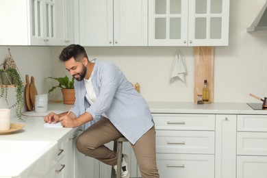 Photo of Handsome young man with notebook sitting on stool in kitchen
