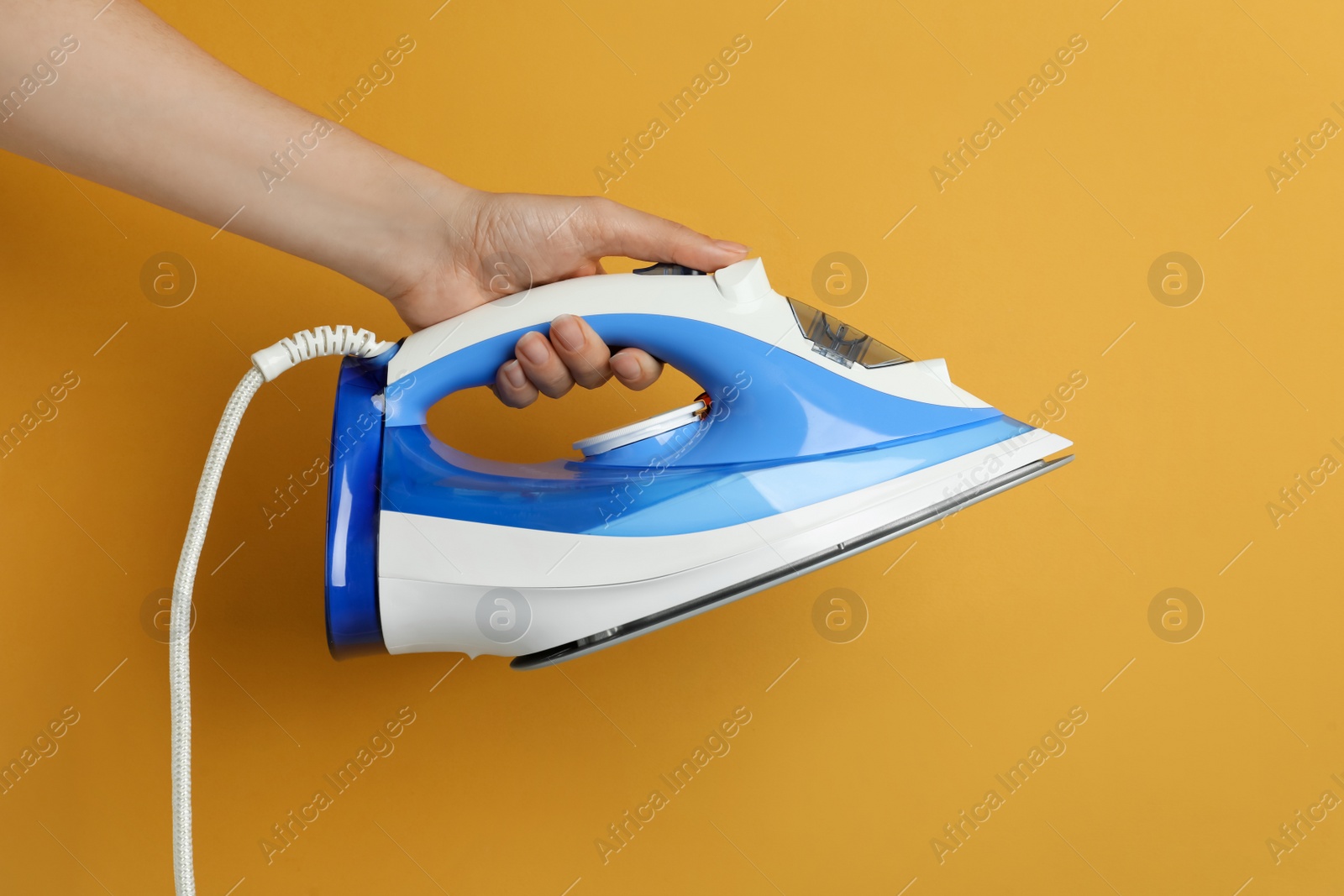 Photo of Woman holding modern iron on orange background, closeup