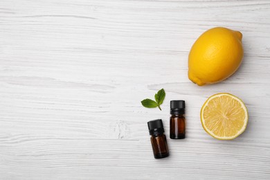 Photo of Bottles of citrus essential oil and fresh lemons on white wooden table, flat lay. Space for text