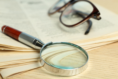 Stack of newspapers, magnifier and glasses on wooden table. Search concept