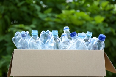 Photo of Cardboard box with used plastic bottles outdoors. Recycle concept