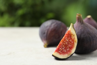 Whole and cut ripe figs on light table against blurred green background, closeup. Space for text