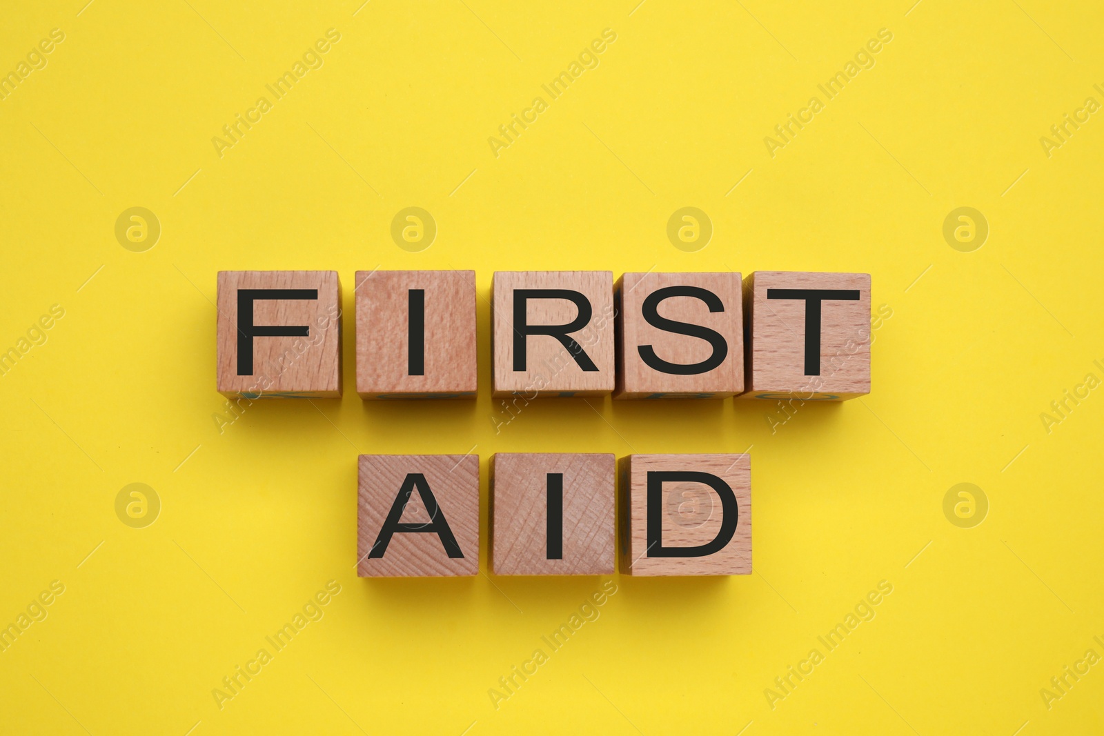 Photo of Words First Aid made of wooden cubes on yellow background, flat lay