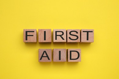 Words First Aid made of wooden cubes on yellow background, flat lay