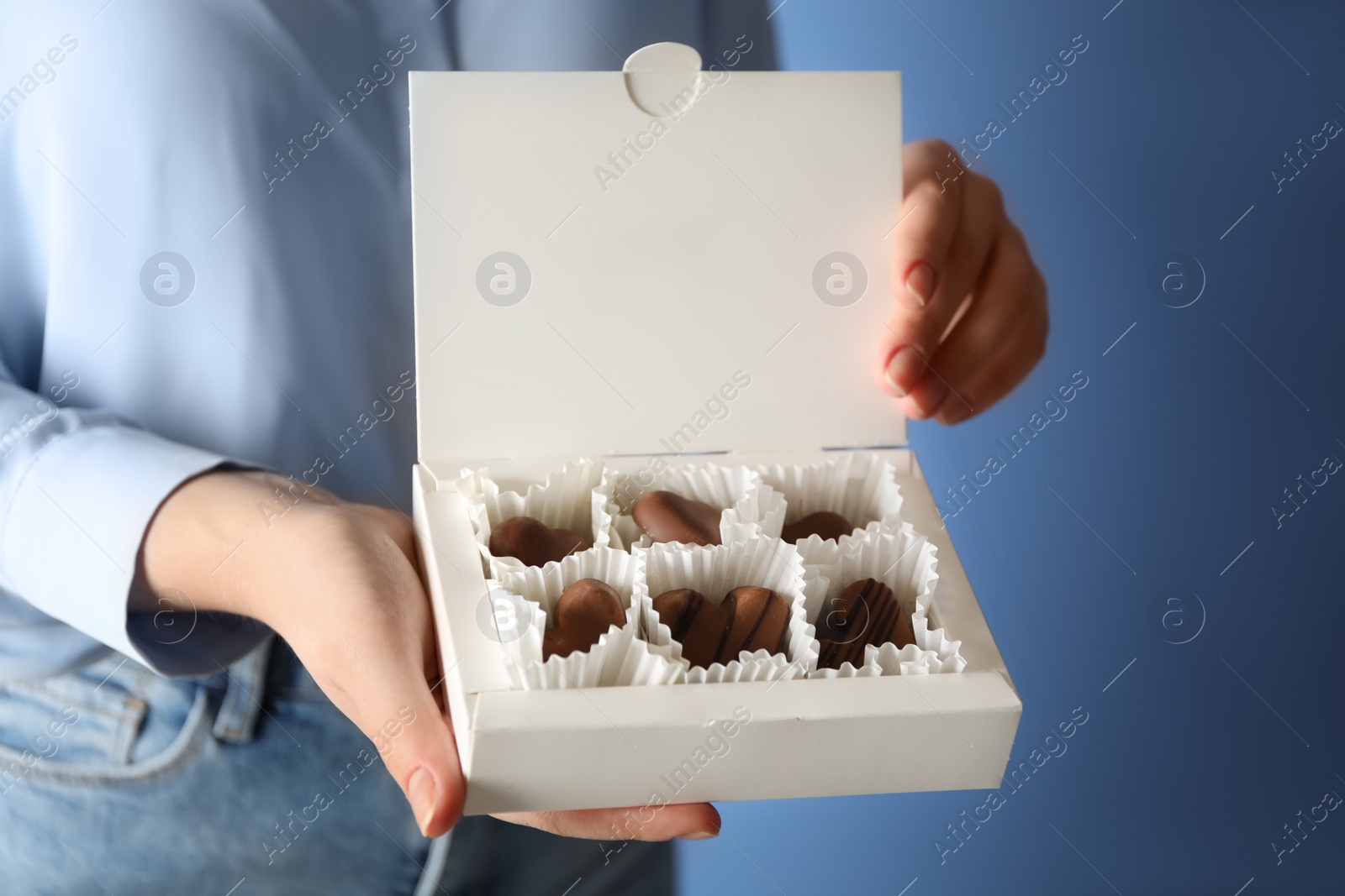 Photo of Woman with box of heart shaped chocolate candies on blue background, closeup