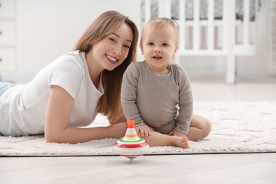 Photo of Children toys. Happy mother with her little son and spinning top on rug at home