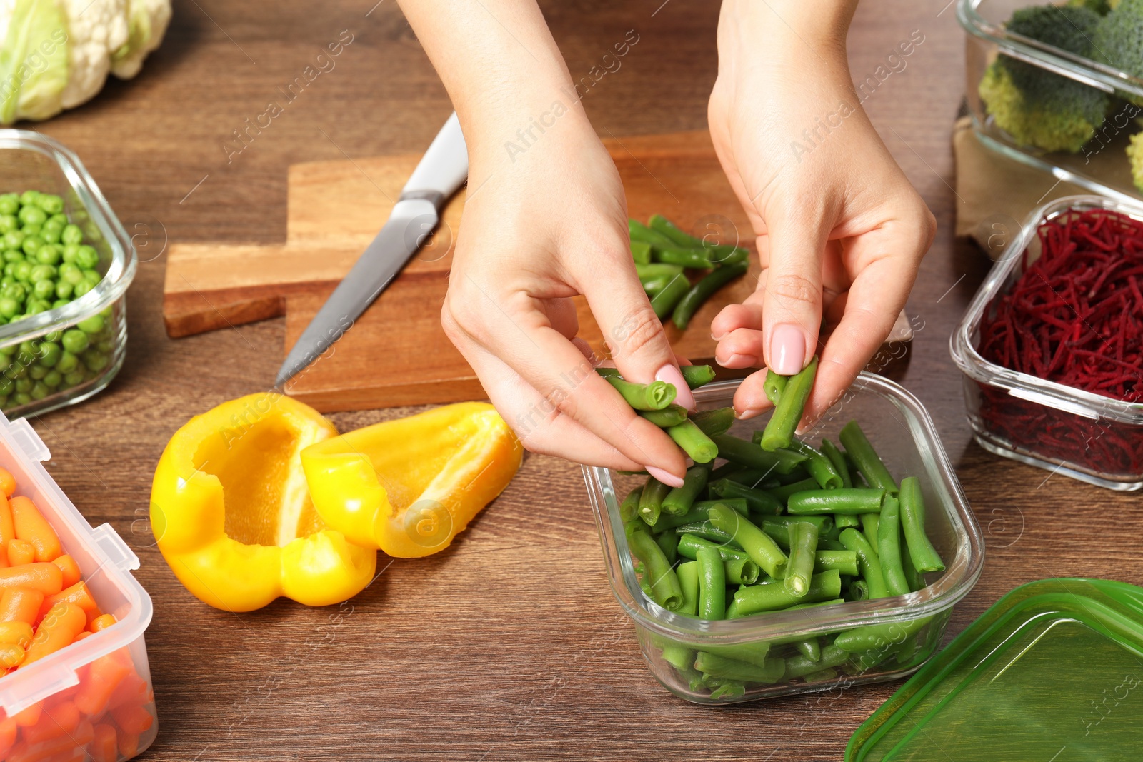 Photo of Woman putting green beans into glass container at wooden table, closeup. Food storage