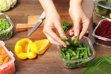 Woman putting green beans into glass container at wooden table, closeup. Food storage