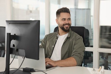 Happy man working on laptop in open plan office