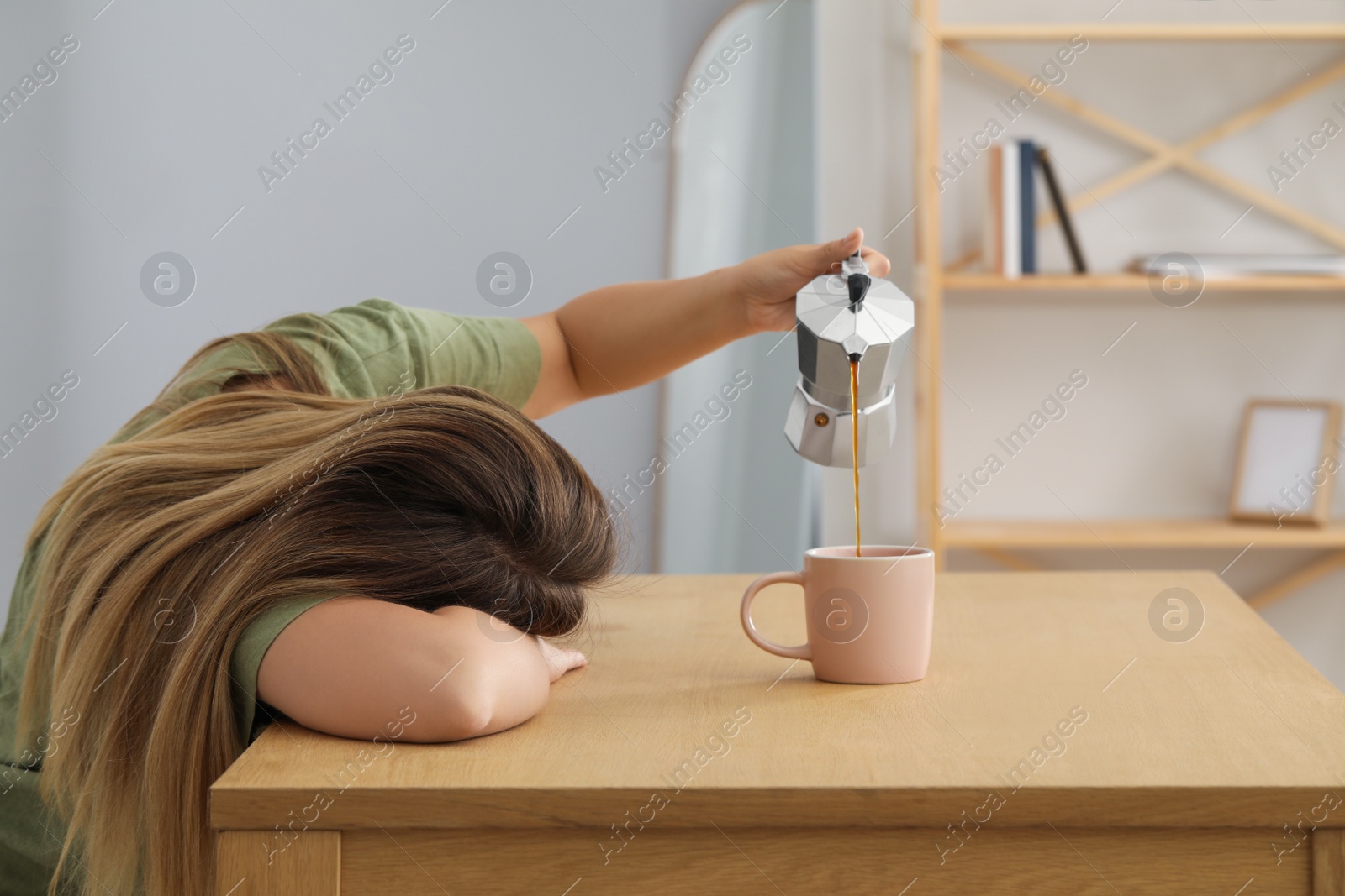 Photo of Sleepy woman pouring coffee into cup at wooden table indoors