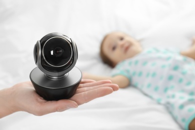 Photo of Woman holding baby camera near child on bed. Video nanny