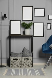 Photo of Stylish room interior with empty frames hanging on grey wall near console table