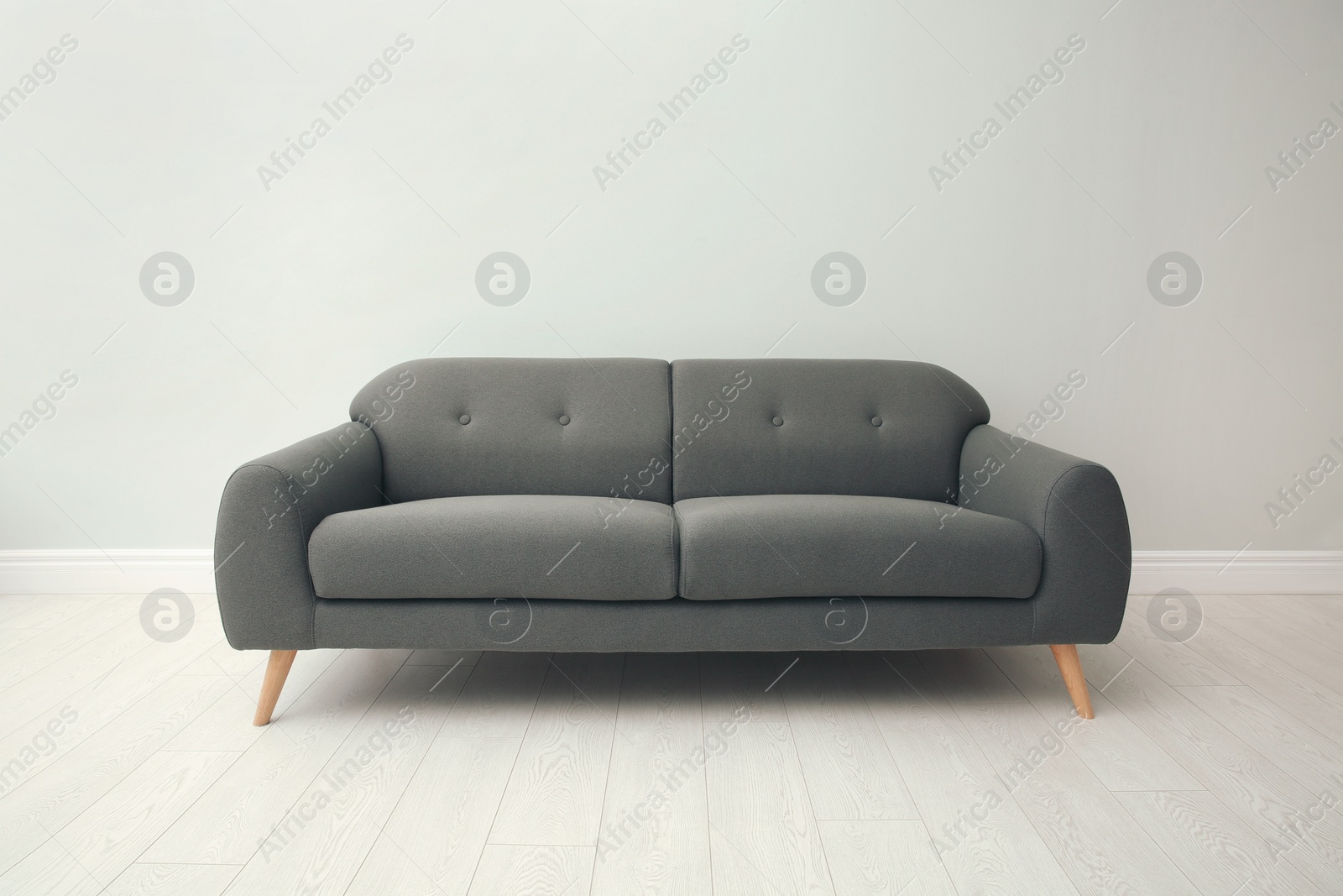 Photo of Comfortable grey sofa near white wall indoors. Interior design