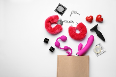 Paper shopping bag with different sex toys on white background, top view