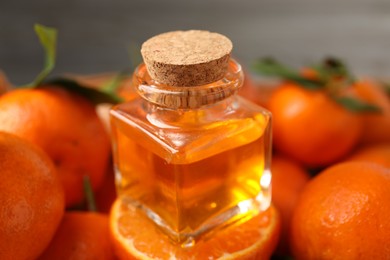 Photo of Bottle of tangerine essential oil with fresh fruits on grey background, closeup