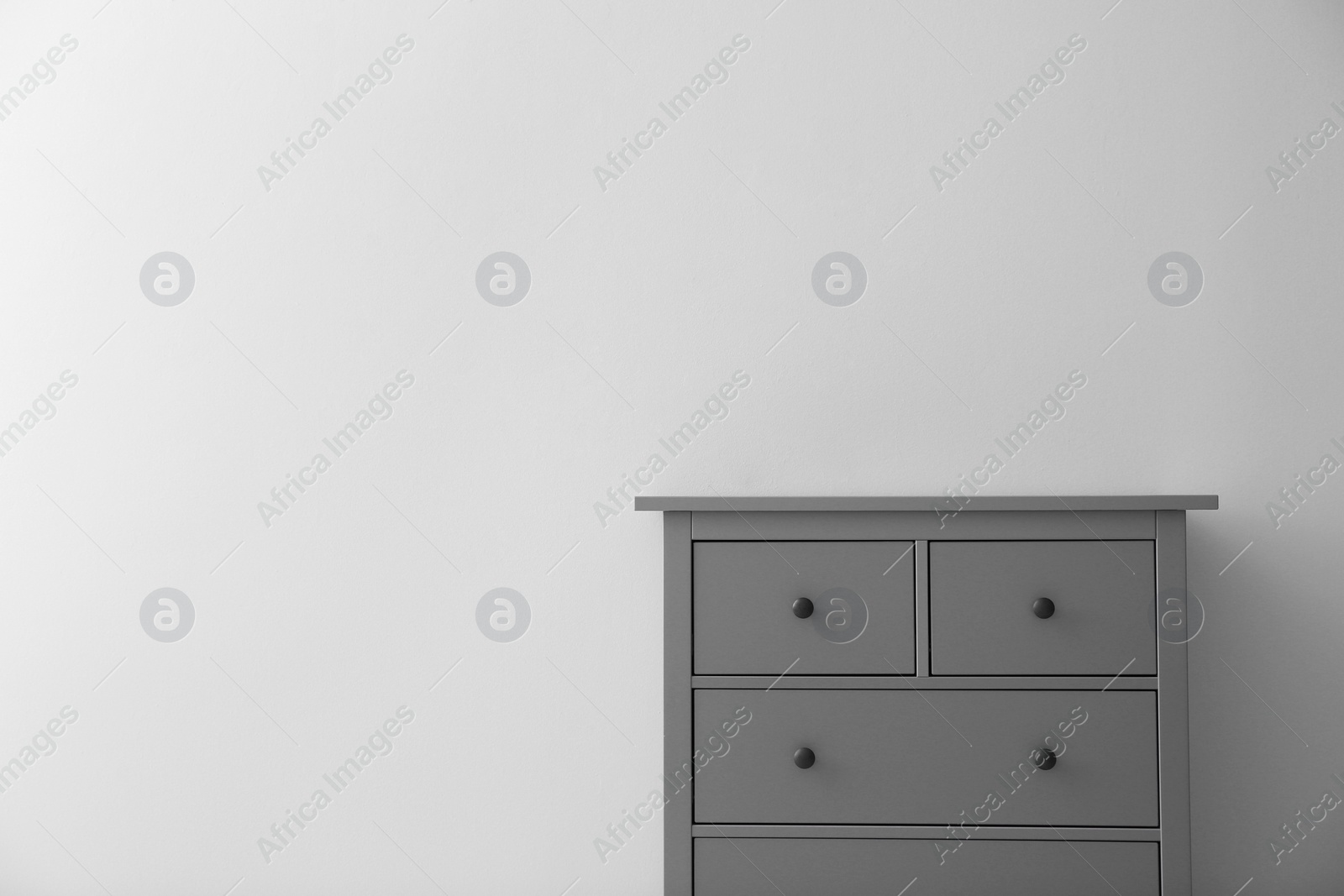 Photo of Modern grey chest of drawers near light wall in room, space for text. Interior design