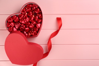 Photo of Box of heart shaped chocolate candies and ribbon on pink wooden table, flat lay. Space for text