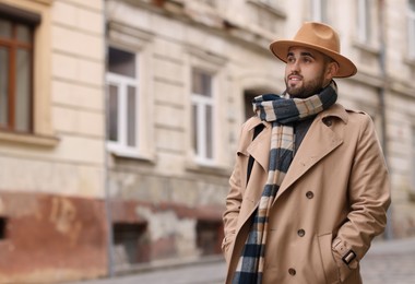 Photo of Smiling man in warm scarf on city street. Space for text