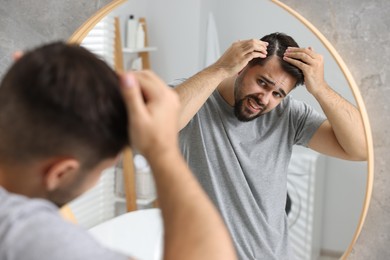 Photo of Emotional man with dandruff in his dark hair near mirror in bathroom