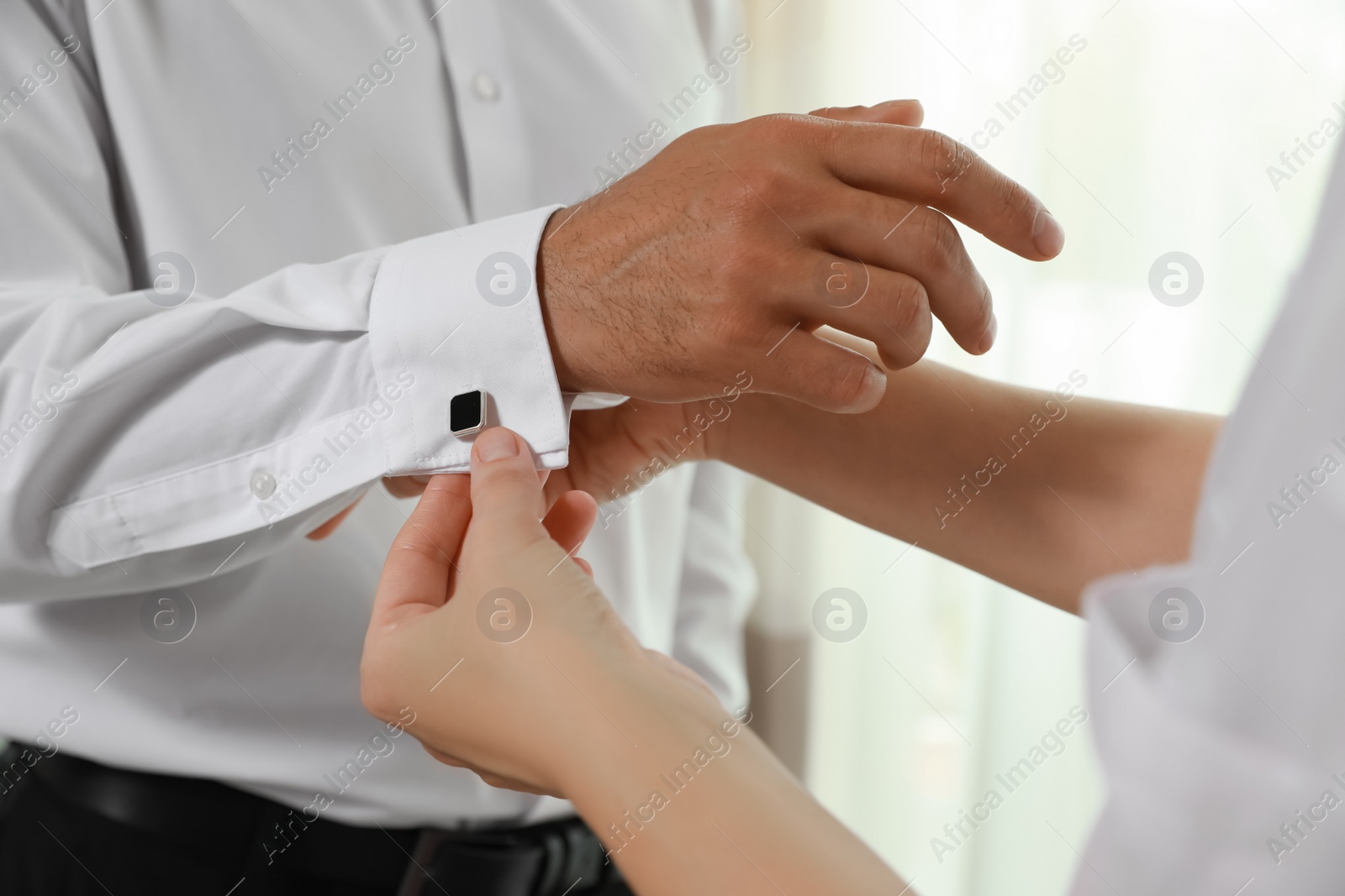 Photo of Woman helping man to put on cufflink, closeup