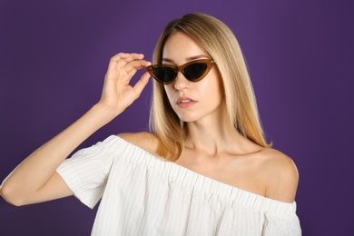 Beautiful woman in stylish sunglasses on purple background