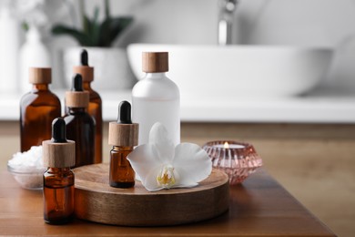 Photo of Essential oils, orchid flower and sea salt on wooden table in bathroom