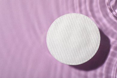 Photo of Cotton pad and micellar water on violet background, top view. Space for text