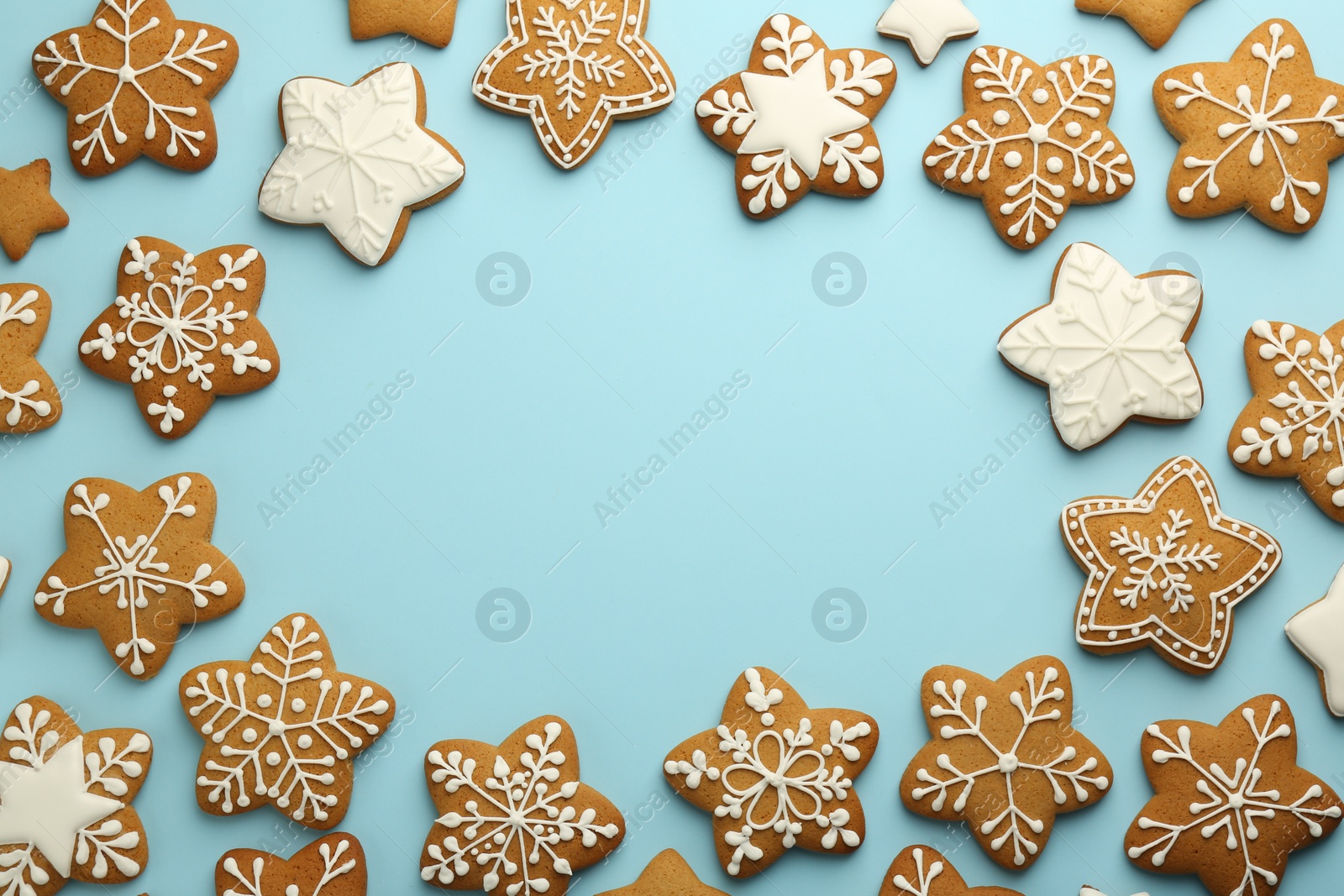 Photo of Frame made of tasty star shaped Christmas cookies with icing on light blue background, flat lay. Space for text