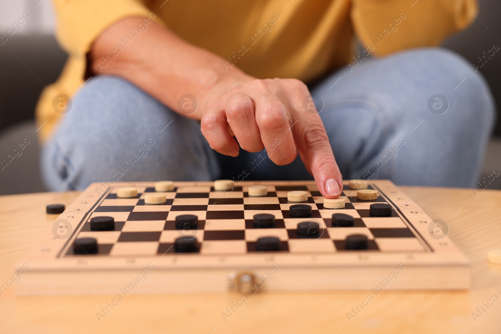 Photo of Woman playing checkers at wooden table, closeup