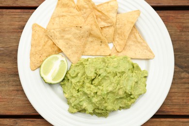 Delicious guacamole made of avocados, nachos and lime on wooden table, top view