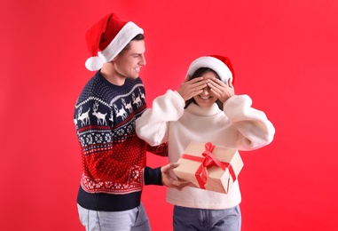 Photo of Man presenting Christmas gift to his girlfriend on red background