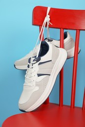 Pair of stylish sneakers hanging on red chair against light blue background