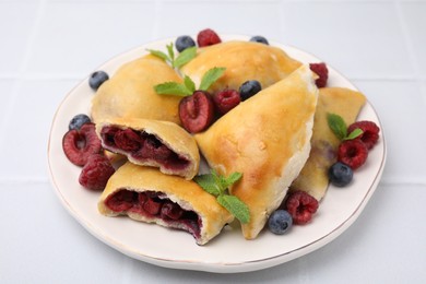 Photo of Plate of delicious samosas, berries and mint leaves on white tiled table