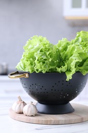 Fresh lettuce in black colander on white marble table in kitchen, closeup