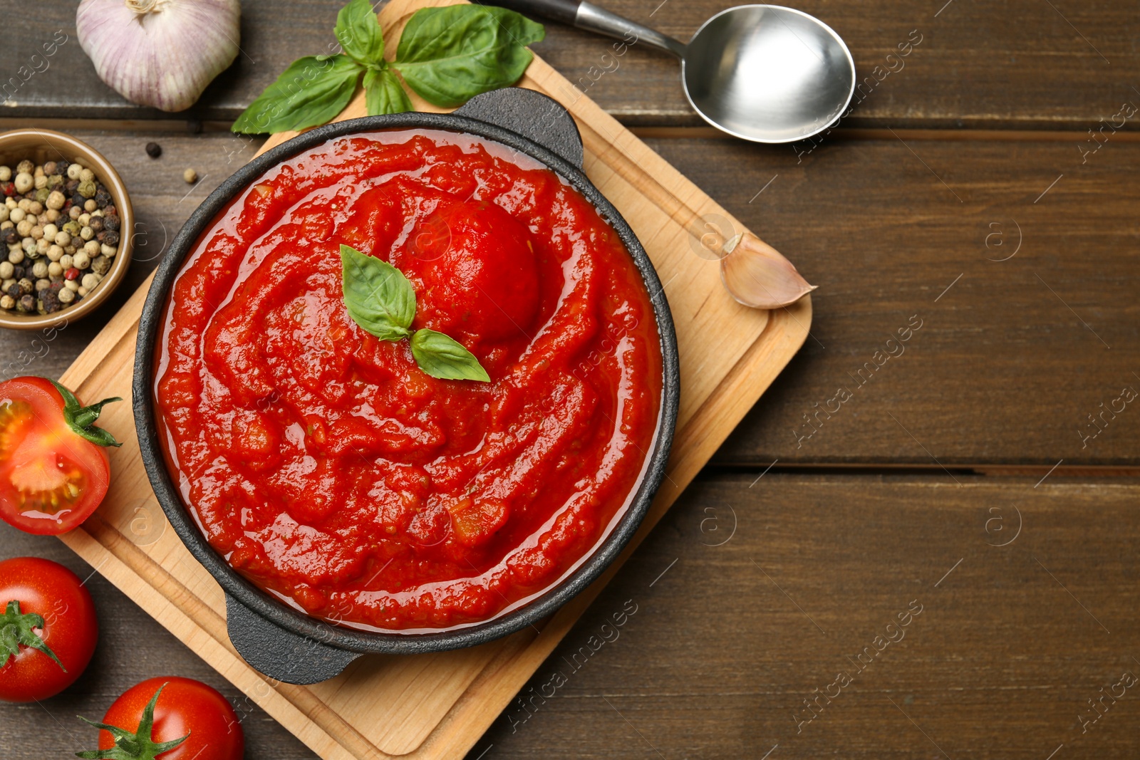 Photo of Homemade tomato sauce in bowl, spoon and ingredients on wooden table, flat lay. Space for text