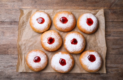 Photo of Hanukkah doughnuts with jelly and sugar powder on wooden table, flat lay