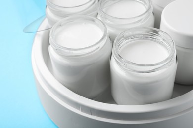 Photo of Modern yogurt maker with full jars on light blue background, closeup