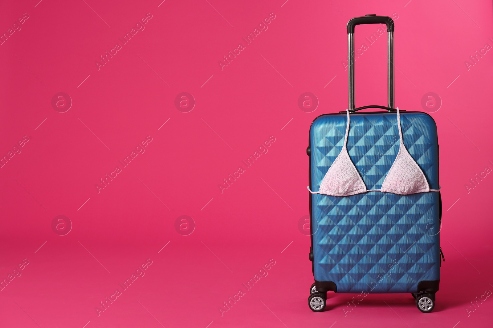 Photo of Stylish suitcase with bikini top on color background. Space for text